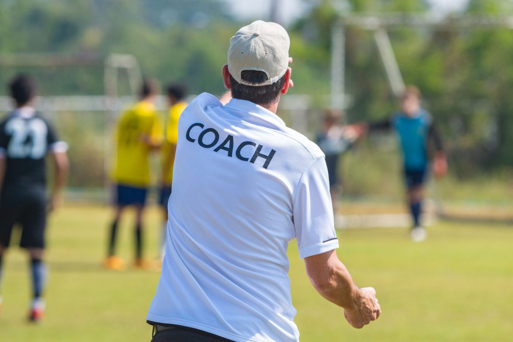 Back of sport coach wearing COACH shirt at an outdoor sport fiel